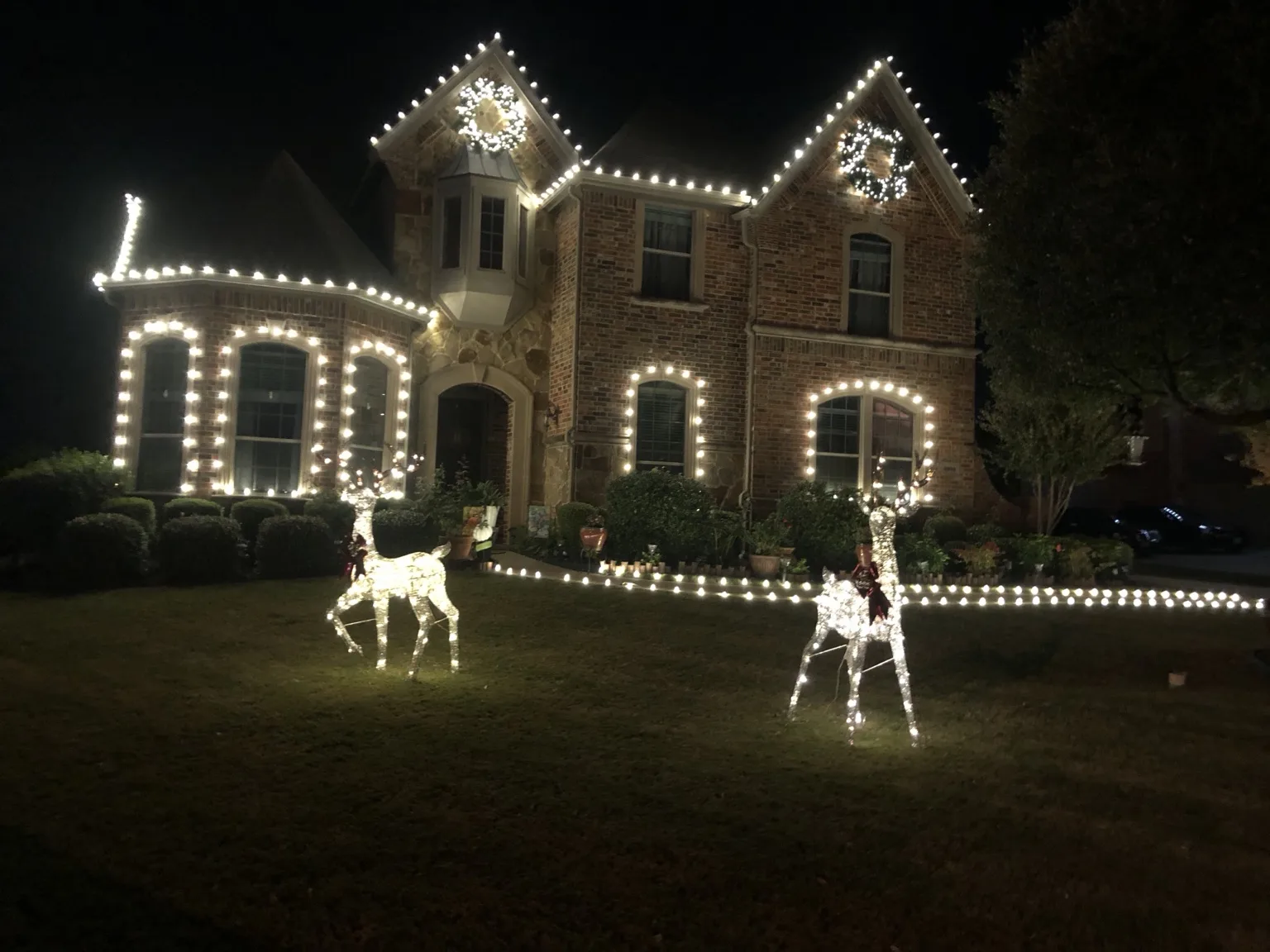 Multicolor Christmas lights outlining a two-story home and garage with a wreath