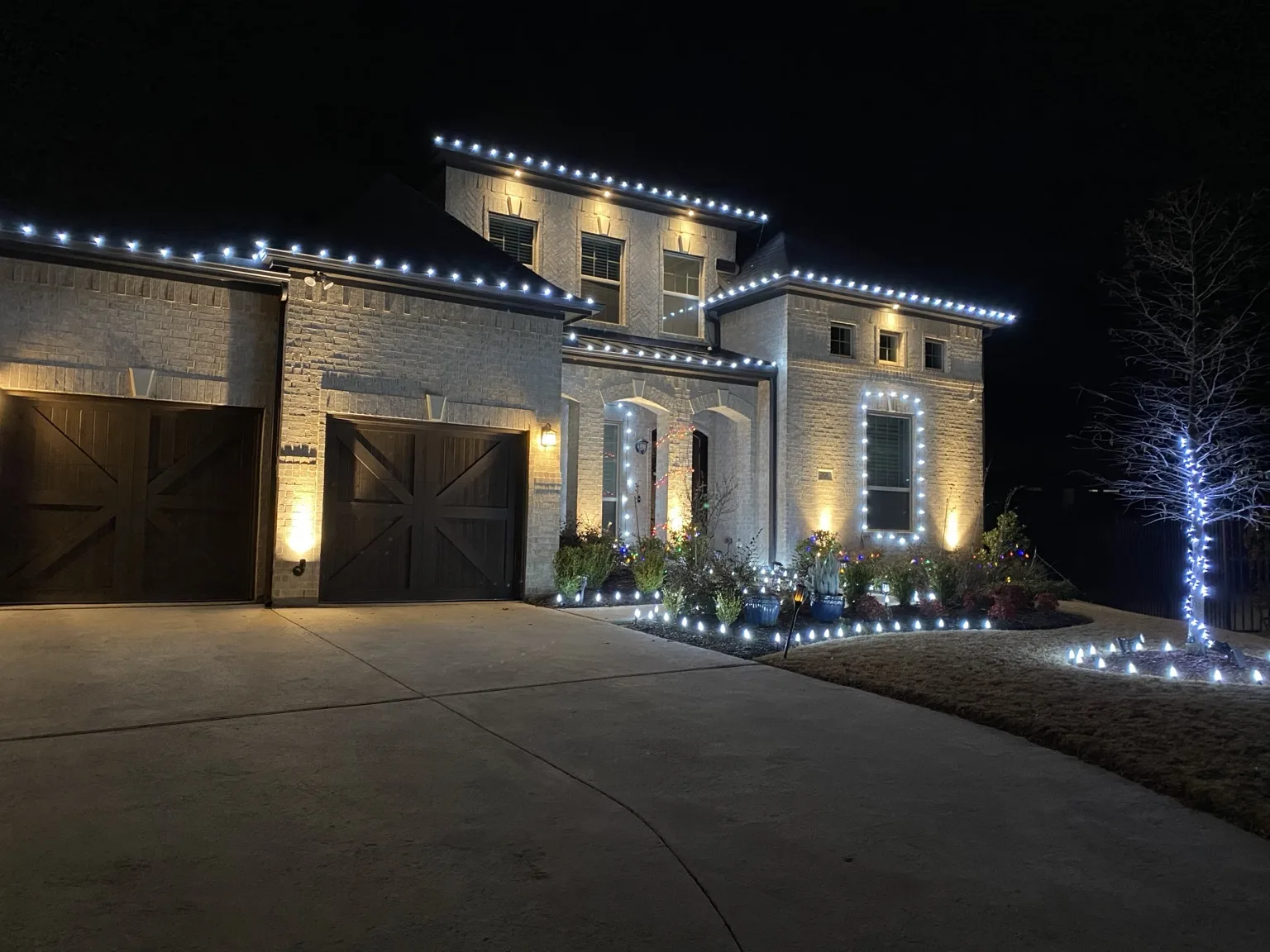 Cool white Christmas lights outlining a modern two-story home and landscape